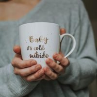 Close-up of a woman holding a mug reading 'Baby it's cold outside' indoors, cozy winter vibe.